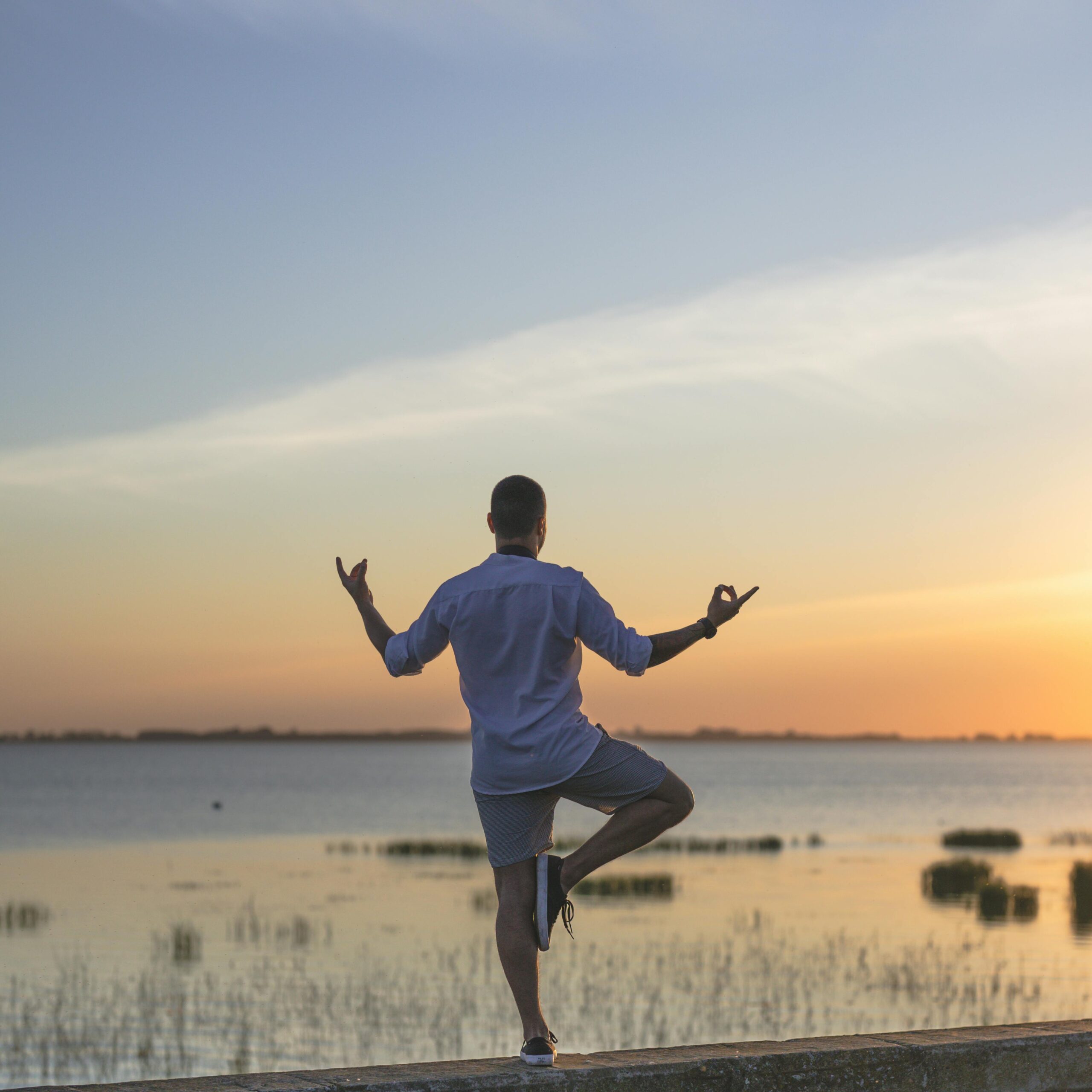 A man practices yoga by a serene lake during a beautiful sunset in Chascomús, Argentina.